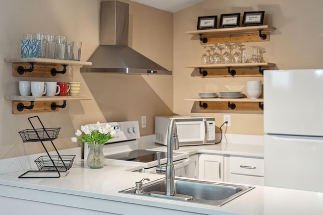 kitchen with white cabinets, white appliances, vaulted ceiling, and wall chimney range hood