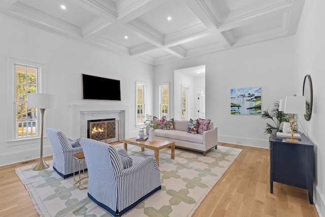 living room featuring beam ceiling, light wood-style flooring, a fireplace with flush hearth, coffered ceiling, and baseboards