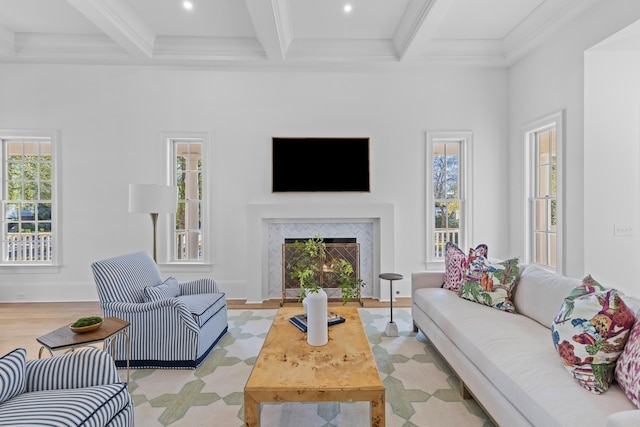 living area with a lit fireplace, ornamental molding, beamed ceiling, and light wood-type flooring