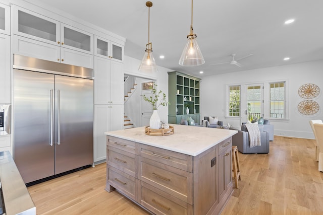 kitchen featuring built in appliances, glass insert cabinets, white cabinetry, and a center island