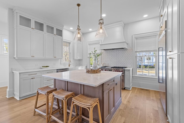 kitchen featuring a kitchen island, white cabinetry, light wood finished floors, glass insert cabinets, and custom range hood