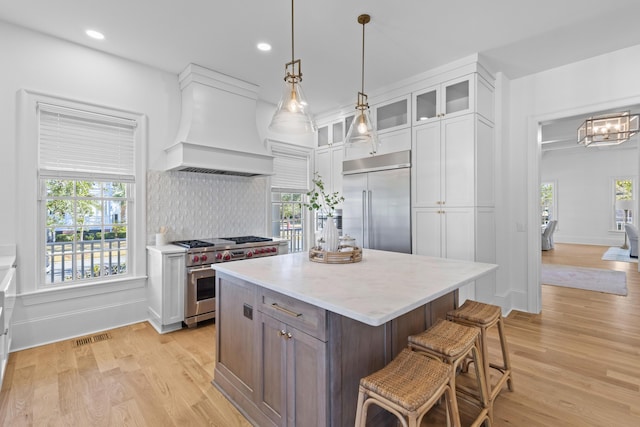 kitchen with premium range hood, a kitchen island, high quality appliances, white cabinetry, and glass insert cabinets