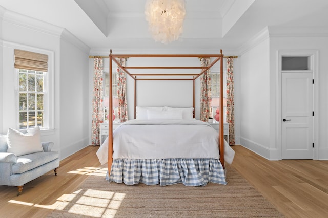 bedroom featuring baseboards, a raised ceiling, crown molding, light wood-style floors, and a chandelier