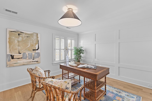 office area with crown molding, light wood finished floors, visible vents, and a decorative wall