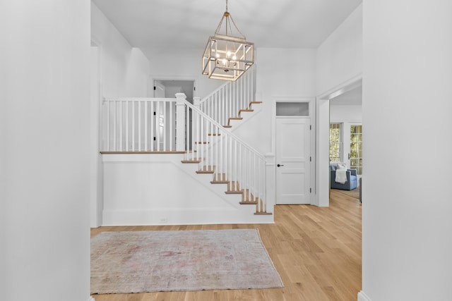 foyer featuring stairs, light wood finished floors, and a chandelier