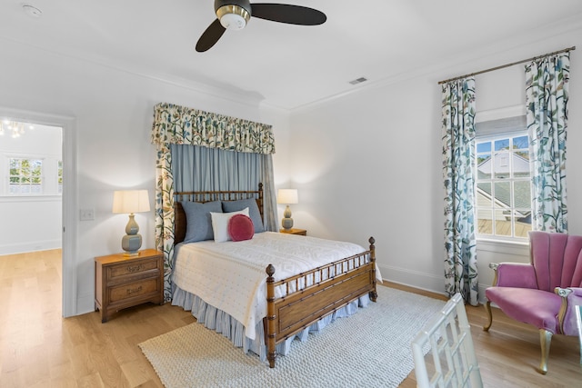 bedroom with a ceiling fan, visible vents, baseboards, ornamental molding, and light wood-type flooring