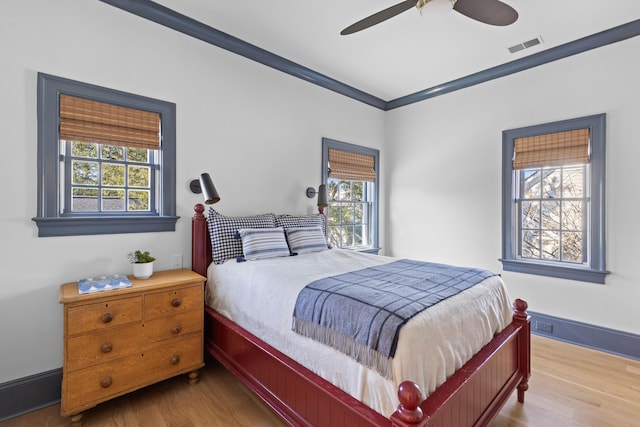 bedroom featuring ornamental molding, multiple windows, wood finished floors, and visible vents