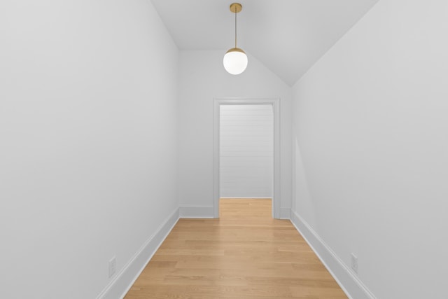 corridor featuring lofted ceiling, baseboards, and light wood-style floors