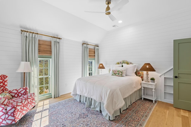 bedroom featuring lofted ceiling, ceiling fan, light wood-style flooring, wood walls, and visible vents