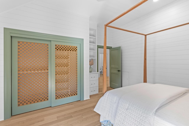 bedroom with light wood-style floors and wooden walls