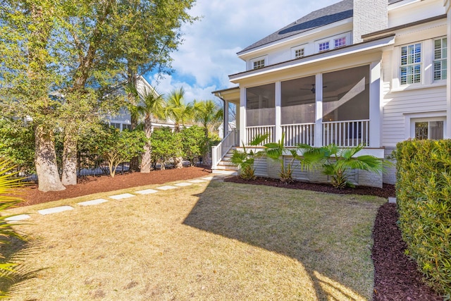 rear view of property with a sunroom, ceiling fan, a chimney, and a lawn