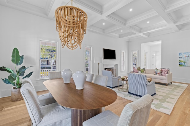 dining area with coffered ceiling, a fireplace, light wood-style floors, beamed ceiling, and an inviting chandelier