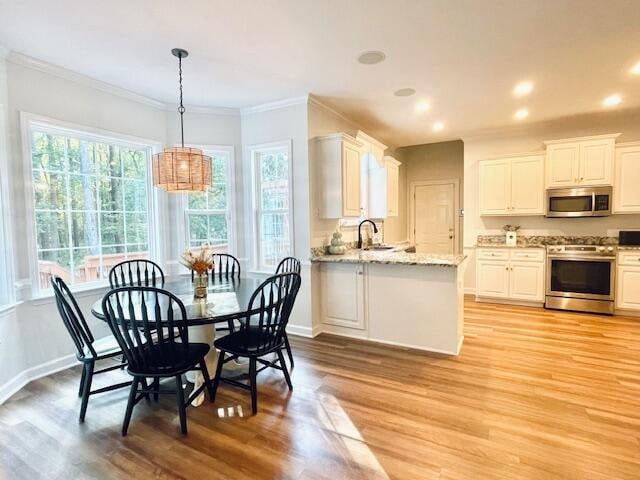 dining space featuring a notable chandelier, crown molding, sink, and light hardwood / wood-style flooring