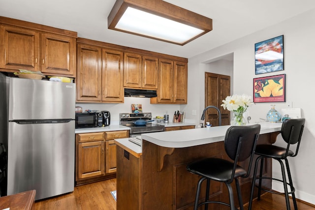 kitchen with light hardwood / wood-style floors, kitchen peninsula, stainless steel appliances, sink, and a breakfast bar area