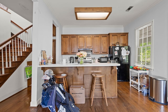 kitchen featuring stainless steel range oven, dark hardwood / wood-style floors, kitchen peninsula, black fridge, and a kitchen bar