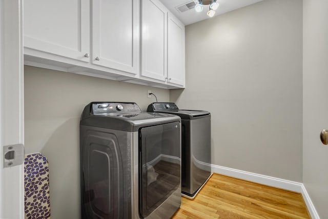 laundry area with washer and clothes dryer, light wood-type flooring, and cabinets