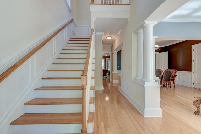 stairs featuring decorative columns, wood finished floors, and ornamental molding