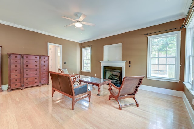 living area featuring light wood-style floors, a ceiling fan, crown molding, a fireplace, and baseboards