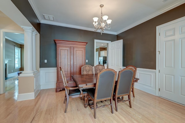 dining area with decorative columns, light wood-type flooring, a chandelier, ornamental molding, and a decorative wall