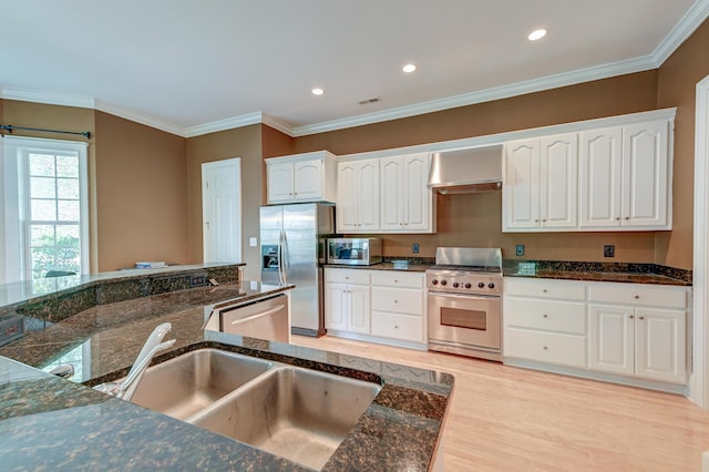 kitchen with appliances with stainless steel finishes, wall chimney exhaust hood, a sink, dark stone counters, and white cabinetry