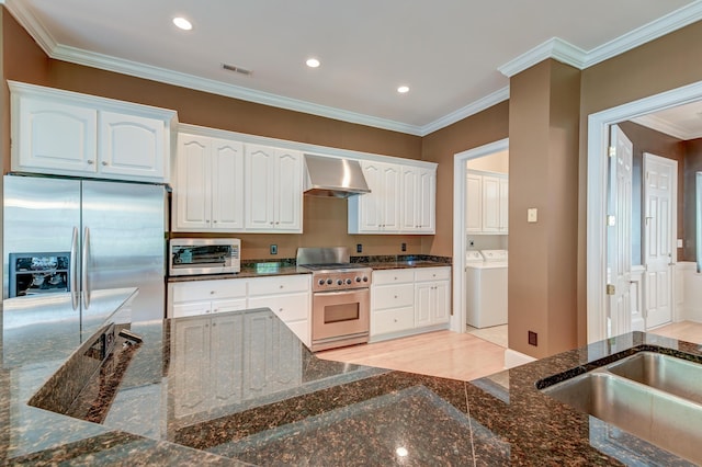 kitchen with stainless steel appliances, wall chimney range hood, dark stone counters, white cabinetry, and crown molding