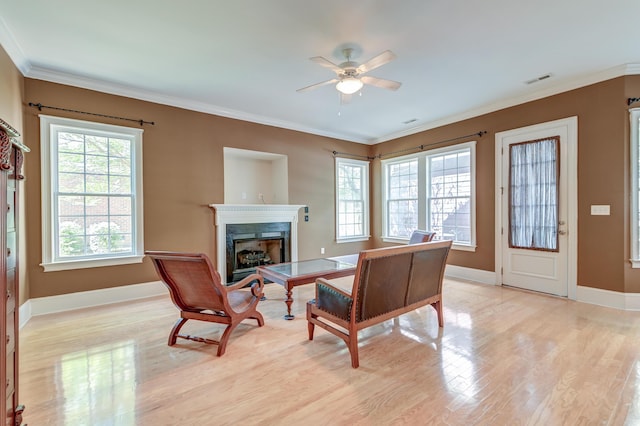 living area with light wood finished floors, a ceiling fan, a premium fireplace, baseboards, and crown molding