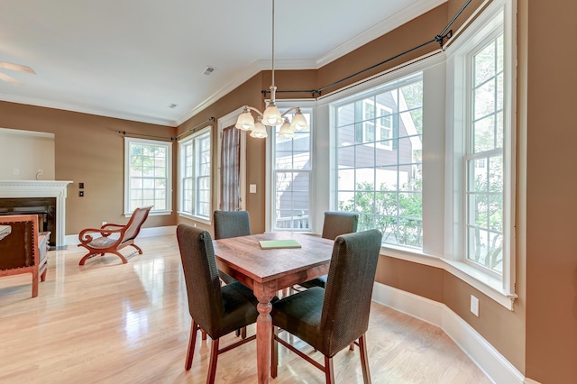 dining space with healthy amount of natural light, a chandelier, light wood-style flooring, baseboards, and ornamental molding