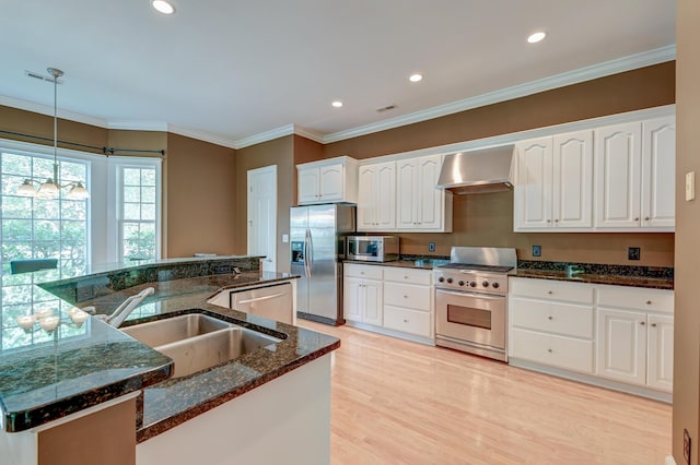 kitchen featuring stainless steel appliances, wall chimney range hood, a sink, hanging light fixtures, and white cabinets