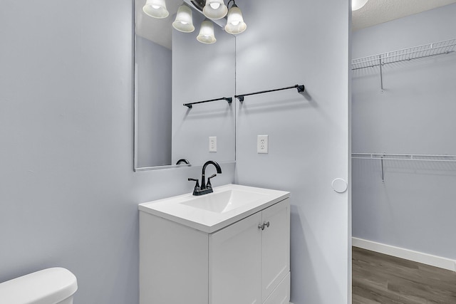 bathroom with vanity, wood finished floors, baseboards, a walk in closet, and toilet