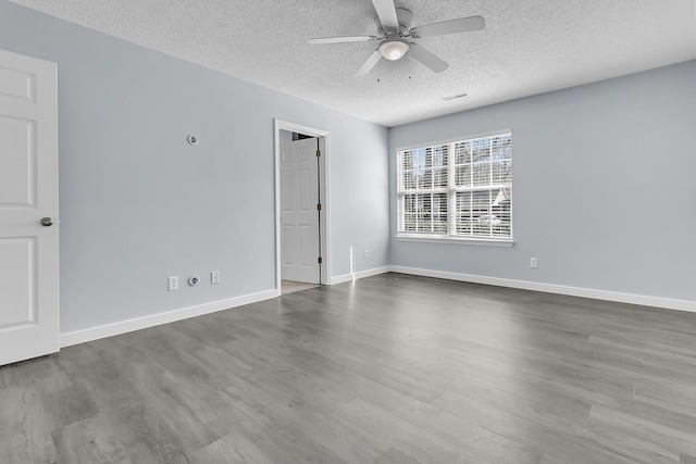 empty room featuring visible vents, a ceiling fan, a textured ceiling, dark wood finished floors, and baseboards