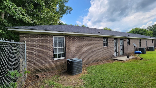 rear view of house with central AC unit and a lawn