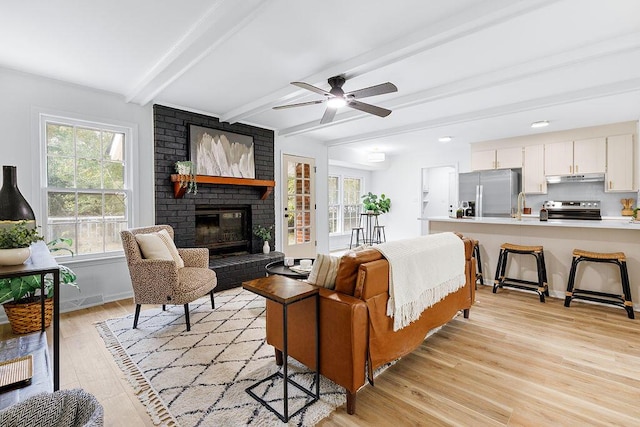 living room with ceiling fan, a fireplace, beamed ceiling, and light hardwood / wood-style floors