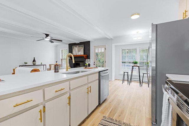 kitchen with white cabinets, sink, light wood-type flooring, appliances with stainless steel finishes, and beamed ceiling