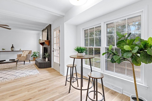 sitting room featuring beam ceiling, a brick fireplace, ceiling fan, and light wood-type flooring