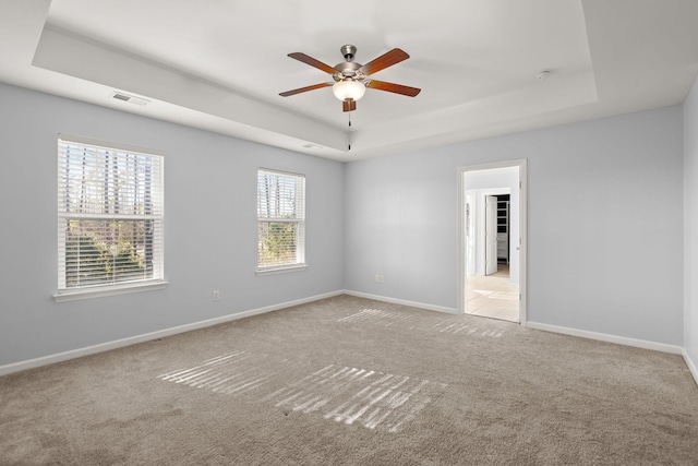 carpeted spare room with ceiling fan, a wealth of natural light, and a raised ceiling