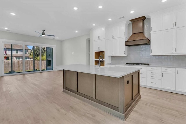 1183 Reserve Ln, Awendaw, SC 29429 - kitchen featuring premium range hood, light wood finished floors, tasteful backsplash, white cabinets, and light countertops
