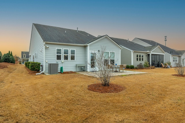 back house at dusk featuring central AC unit, a patio area, and a lawn