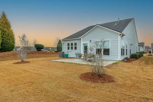 back house at dusk featuring central AC unit, a lawn, and a patio