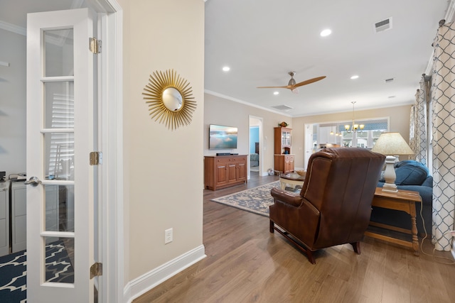 living room with crown molding, ceiling fan with notable chandelier, and light hardwood / wood-style flooring