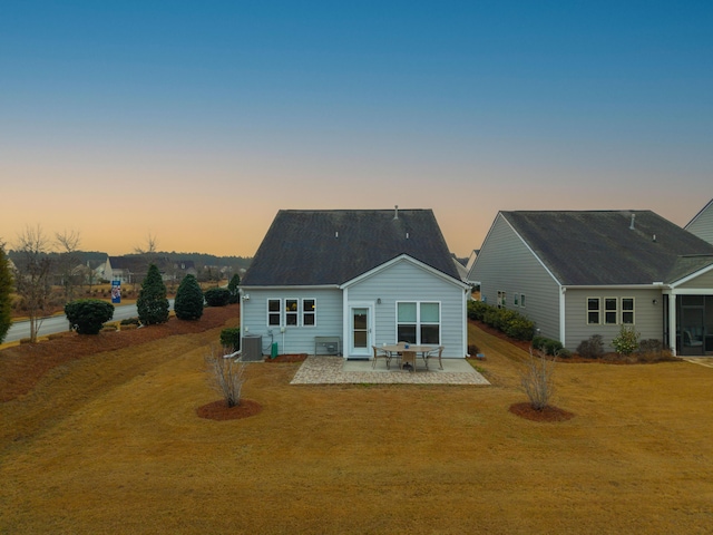 back house at dusk featuring central AC, a yard, and a patio