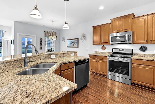 kitchen with sink, hanging light fixtures, light stone countertops, appliances with stainless steel finishes, and dark wood-type flooring