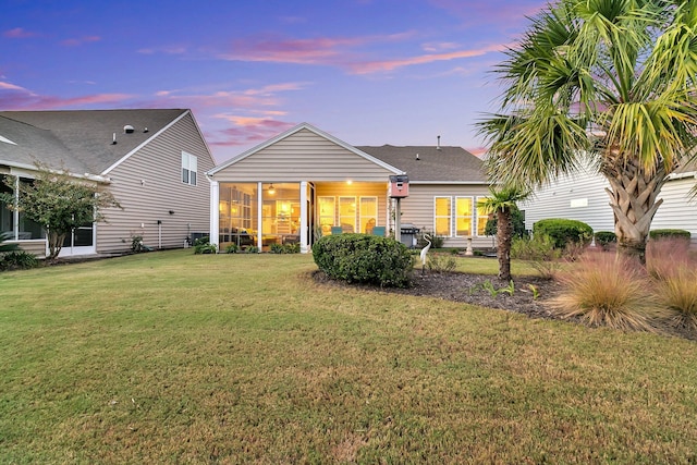 back house at dusk with a sunroom and a lawn