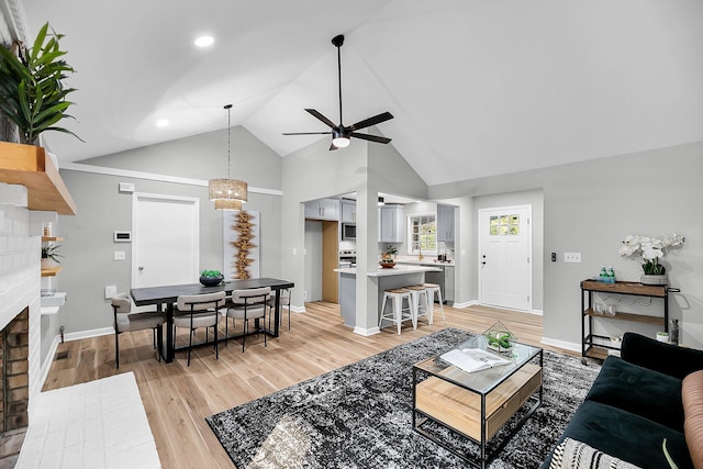 living room featuring baseboards, high vaulted ceiling, light wood-style flooring, a fireplace, and ceiling fan