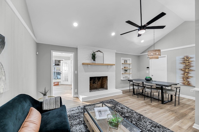 living room featuring light wood finished floors, ceiling fan, built in features, lofted ceiling, and a fireplace