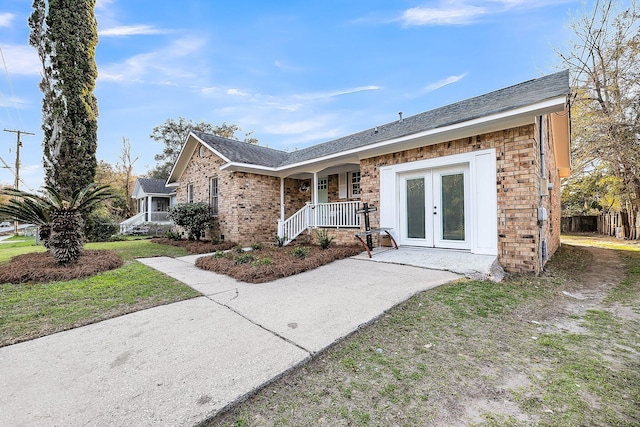 single story home with covered porch, a shingled roof, a front lawn, french doors, and brick siding