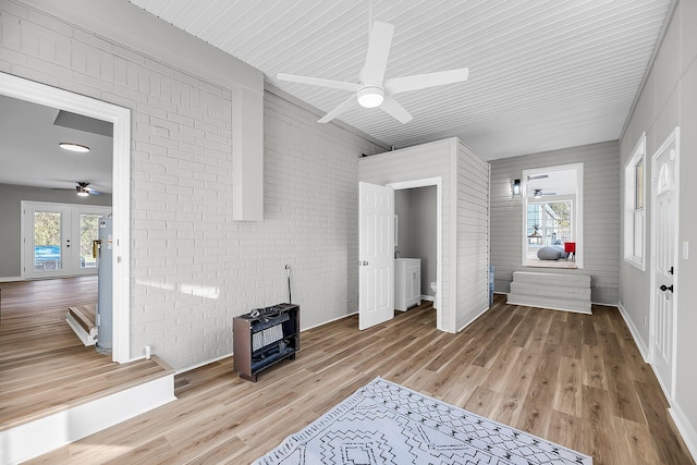 living room with a healthy amount of sunlight, brick wall, a wood stove, ceiling fan, and light wood-type flooring