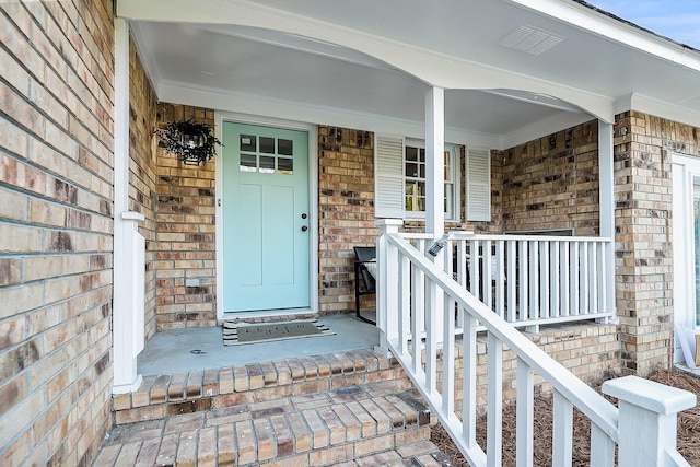 doorway to property featuring a porch and brick siding