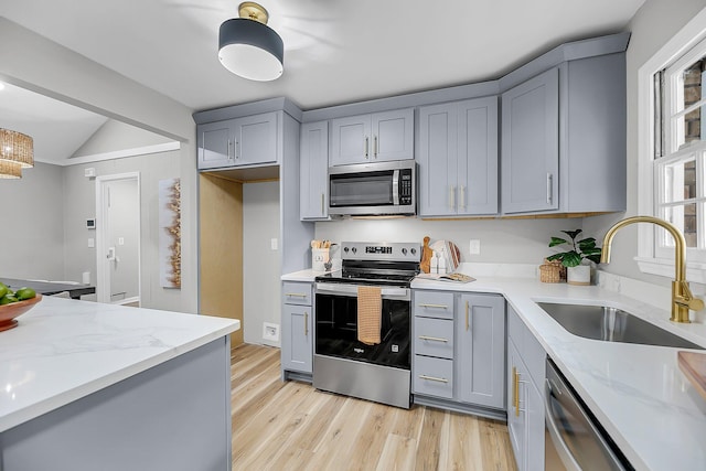 kitchen with gray cabinets, a sink, light stone counters, stainless steel appliances, and light wood-style floors