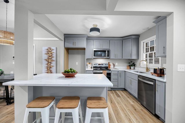 kitchen featuring light wood finished floors, light stone countertops, gray cabinets, stainless steel appliances, and a sink