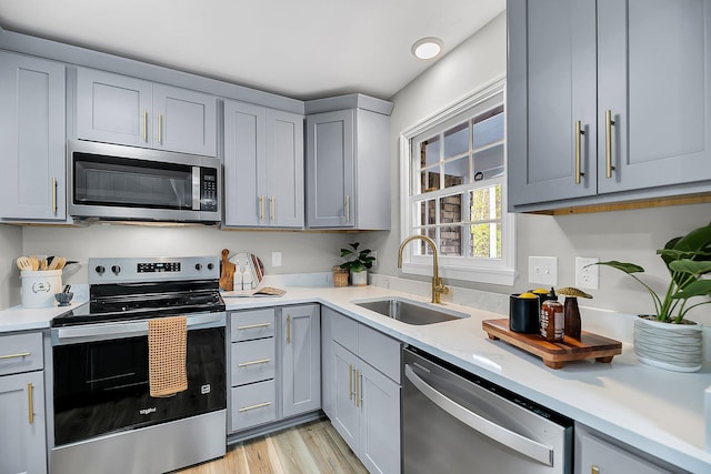 kitchen with light countertops, light wood-style flooring, gray cabinets, stainless steel appliances, and a sink